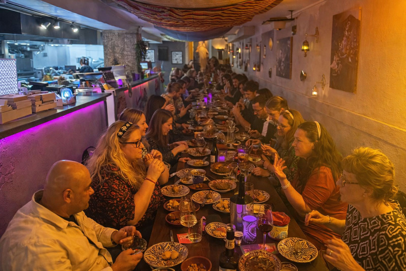 Diverse groep mensen geniet samen van shared dining in restaurant LaSqala in Zwolle, met een tafel vol Mediterrane en Noord-Afrikaanse gerechten.